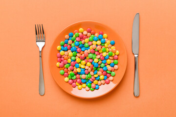cutlery on table and sweet plate of candy. Health and obesity concept, top view on colored background