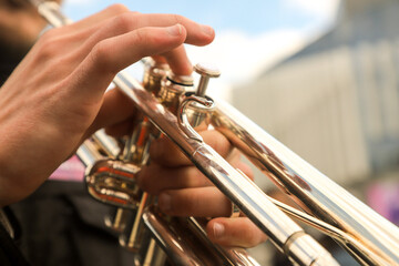 close-up of the hands of a street musician holding a gold-colored pump-action trumpet