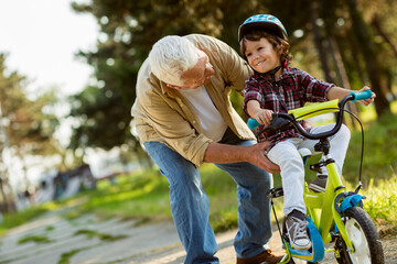 Grandfather and grandson playing in a park and riding a bike
