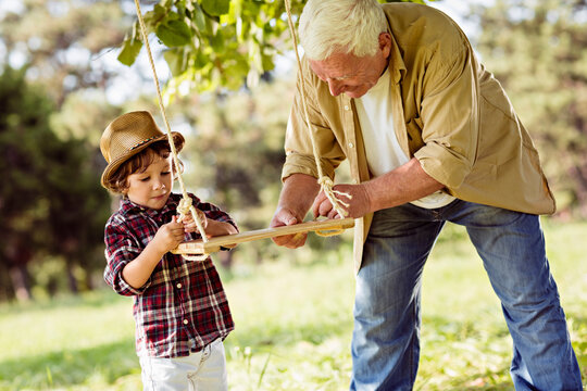 Grandfather And Grandson Playing In A Park With A Swing