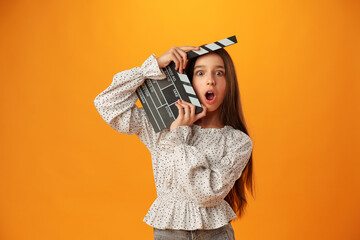 Happy smiling girl portrait holding clapper board on yellow background