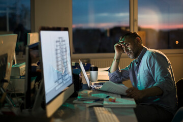 Fototapeta na wymiar Middle aged male architect or designer working overtime at night in a office