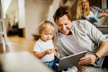 Young father using the tablet and playing with his son in the living room