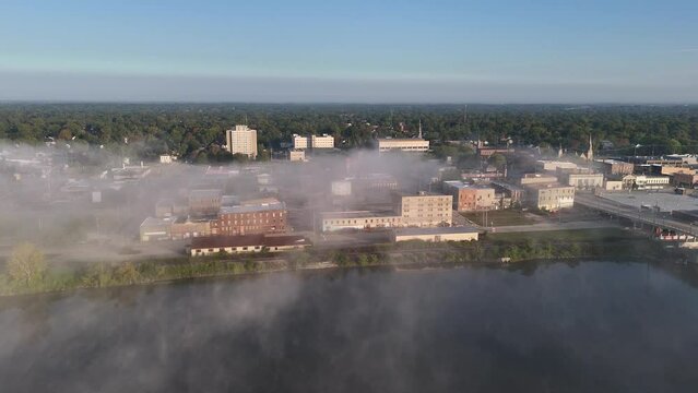 A rising aerial establishing shot of the foggy Saginaw, Michigan skyline.  	