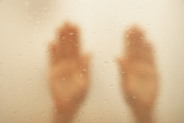 Fototapeta na wymiar Women's hands on the wet glass in the shower close-up, the girl bathes in the shower, her hand