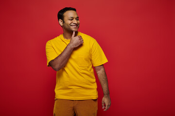 happy indian man in bright casual clothes standing and smiling on red background in studio