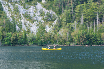 A young couple in a yellow canoe in the middle of Lake Bohinj, Slovenia, with a forest and falling...