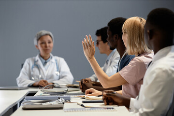 Obraz premium Focus on young blond female assistant raising hand to ask question to coach or experienced general practitioner at seminar or training