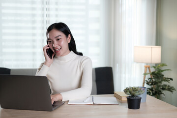 Cheerful young Chinese business woman talking on phone working in modern office.