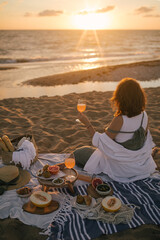 Young woman having beautiful tasty picnic with lemonade, fresh fruits and croissants on a beach at sunset.