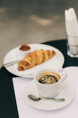 Cup of black coffee and a croissant on a table in a street cafe.