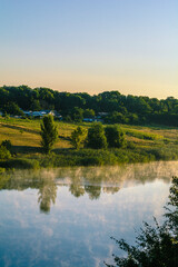 a calm blue lake, over which hangs a thick fog, which is illuminated by the rays of the early sun, against the backdrop of a dark blue sky