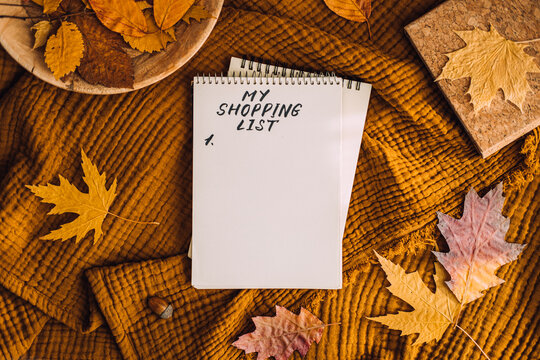 Black Friday, autumn fall season sale, autumn shopping. Shopping List in notebook notepad with autumn leaves, tea coffee cup at brown background in home. Shopping Preparation Consumer Buying