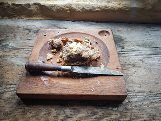An old square wooden trencher with crumbs of bread and cheese on it, an antique knife is laid across the bowl.