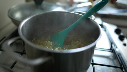 Cooking pasta inside boiling water in metal pan at kicthen stove detail close-up. Ensuring Al Dente...