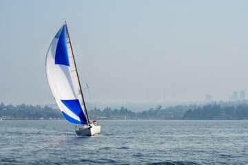 Sailboat sailing spinnaker on smoke filled hazy sky day north of Seattle in Puget Sound.