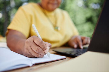 Closeup of Black senior woman writing in planner while working with laptop outdoors, copy space