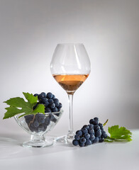 Rose wine in a glass and dark grapes on a light background