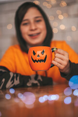 Portrait of candid authentic zoomer boy posing with jack lantern mug and sweets at halloween party