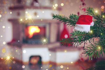 Fototapeta na wymiar Christmas hat on fir tree branch and blur burning fireplace background.