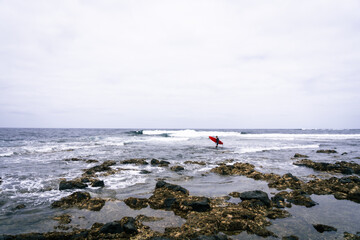 happy surfer in the coast with his red surfboard