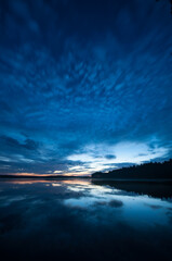 Blue evening colors and cloud formations reflected on the surface of a calm lake in the forests of Finland