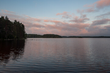 Fototapeta na wymiar Early morning by a lake in Finland with clouds colored pink