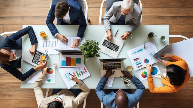 Businesspeople are using wireless technology to collaborate on a project or hold a business meeting. A diverse team brainstorms in a meeting from above. The team is developing a social media strategy.