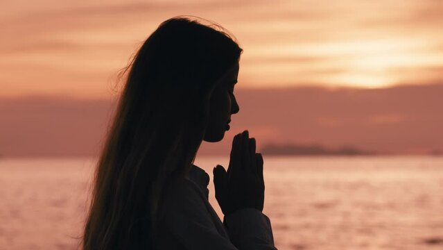 Portrait of young woman praying at sea sunset or sunrise. Female doing yoga prayer pose on sunset beach. Spiritual growth. Concept of religion, spiritual and hope concept