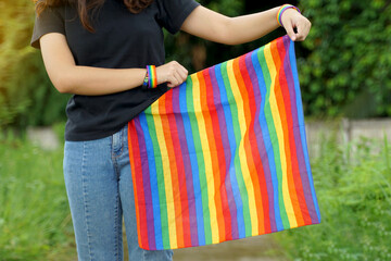 An Asian woman tucks the end of a rainbow-colored striped cloth around the waist of her jeans,...