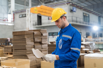 Male warehouse worker working and inspecting quality of cardboard in corrugated carton boxes warehouse storage. Male worker checking cardboard from cardboard making machine