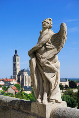 Statue of angel, Kutna Hora, Czech Republic, Czechia - old religious sculpture and church of saint James (Kostel svateho Jakuba) in the background. Sunny and shallow focus.
