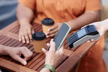 Closeup of unrecognizable person paying via NFC by smartphone at outdoor cafe, copy space
