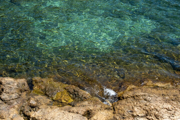 Image of the crystal-clear waters of the Mediterranean Sea in the Costa Brava, with the reflection of the sun on its waves breaking against the rocks.
