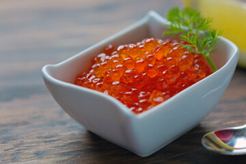 Salmon Red Caviar in ceramic bowl and spoon isolated on wooden background.