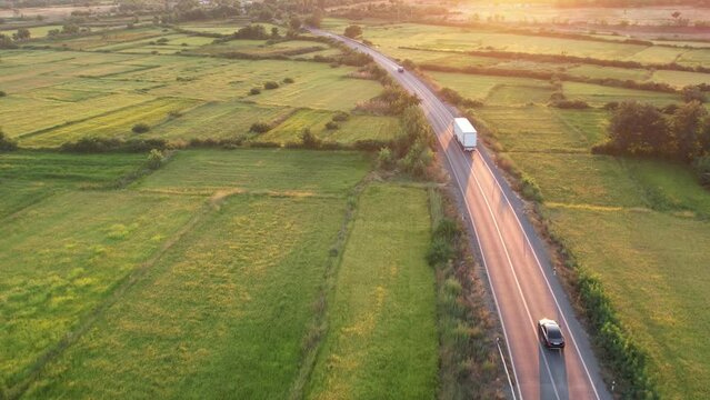 Aerial side shot of a truck with trailer transporting industrial goods on the road in beautiful countryside at sunset