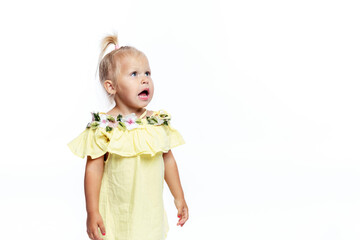 A surprised little girl in a yellow dress stands with her mouth open. Shock and amazement. Isolated on white background. Prsotraanstvo for text.