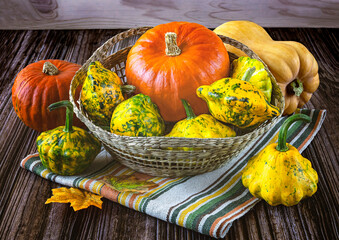 Harvest of ripe yellow and orange pumpkins in basket, autumn leaves, linen striped napkin on wooden...