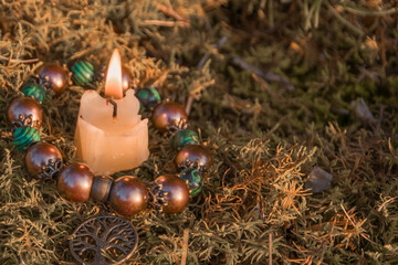 burning candle, a symbol of the moon, an amulet lying on the moss on a dark natural background....