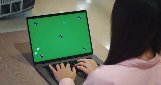 Female working on a laptop with a green screen on the table computer laptop life. female in a cafe or shopping center view over the shoulder looking at green screen computer life remote online work.