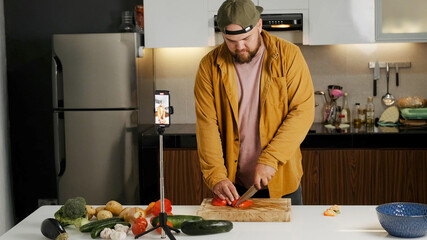 Medium shot, a video blogger in a shirt records himself on his phone and tells the camera a recipe for cooking a dish. A food blogger is cooking in her kitchen at home, isolation concept.