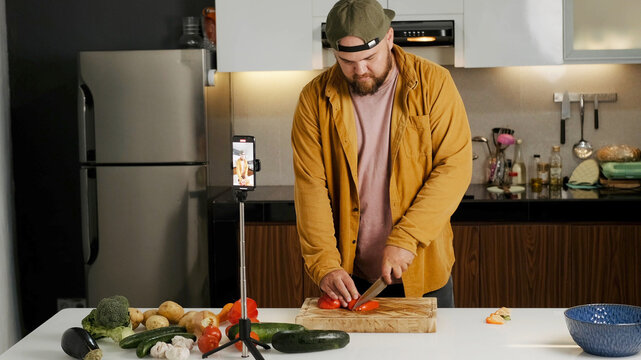Medium shot, a video blogger in a shirt records himself on his phone and tells the camera a recipe for cooking a dish. A food blogger is cooking in her kitchen at home, isolation concept.