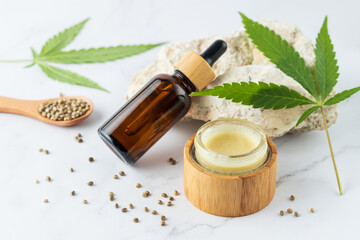Hemp salve for joints and muscles in open glass wooden jar and relaxing CBD serum oil in glass...