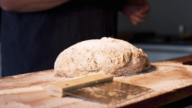 Hands folding and kneading bread dough on a wooden work surface with flour. Close-up. Background for the bakery craft.