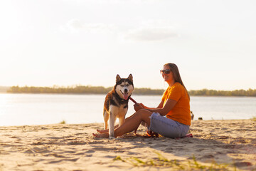 Woman in sunglasses sits with her dog on the beach and enjoying sunset
