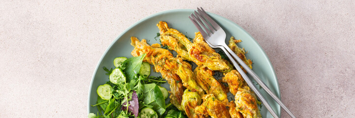 Fried zucchini flowers in batter, a plate with zucchini flowers on a dark background, top view