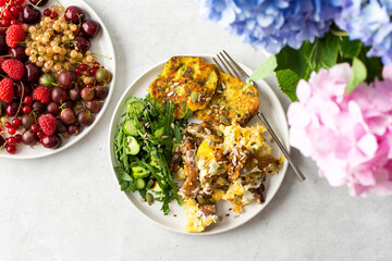 Healthy breakfast, scrambled eggs with fried mushrooms Chanterelles, salad with arugula, cucumbers and various seeds, fried zucchini pancakes, a plate with berries and a bouquet of hydrangeas