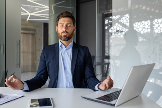 Mature successful senior experienced man meditating in lotus position inside office, businessman with closed eyes resting and visualizing future plans, boss in business suit at workplace