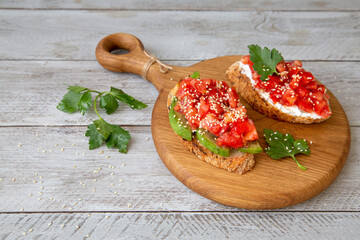 Bruschetta with cottage cheese, avocado, tomatoes, greens, white sesame seeds. Healthy food, rich in healthy fats, fiber, vitamins, antioxidants. Vegetarian food.