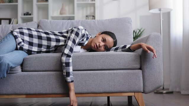 Tired african american girl slumps on couch feeling lethargic. Feeling depressed, lack of motivation, sadness, boredom. Exhausted, she collapses on the couch from stress. Burn out.